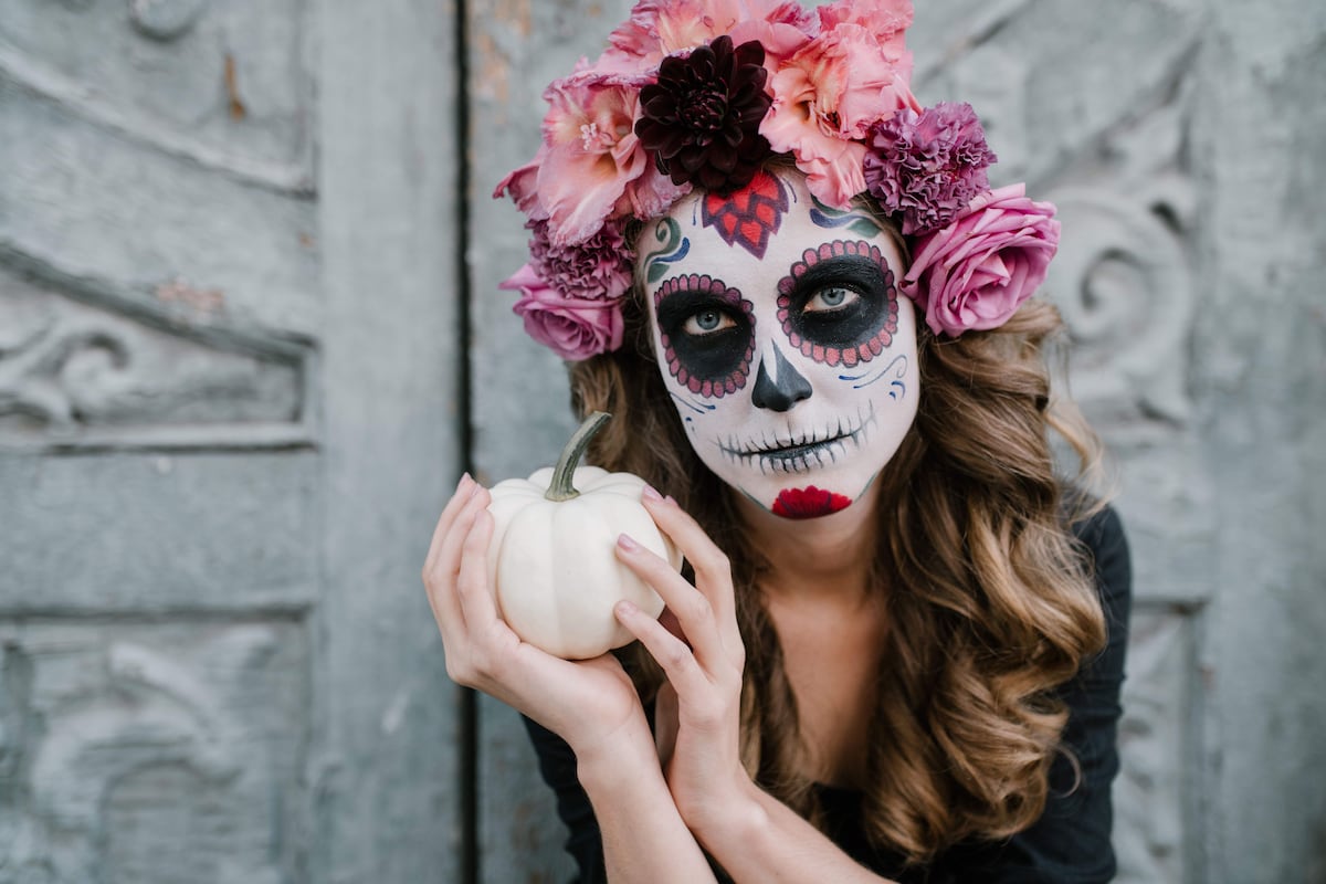 Mujer maquillada de Catrina con flores en el cabello y una calabaza blanca en las manos